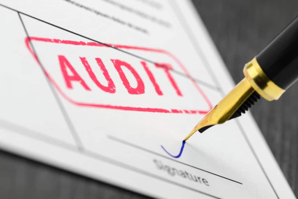 Deze foto beschrijft een auditor die een handtekening zet onder een auditrapport van een financial audit. Via ARC People.
